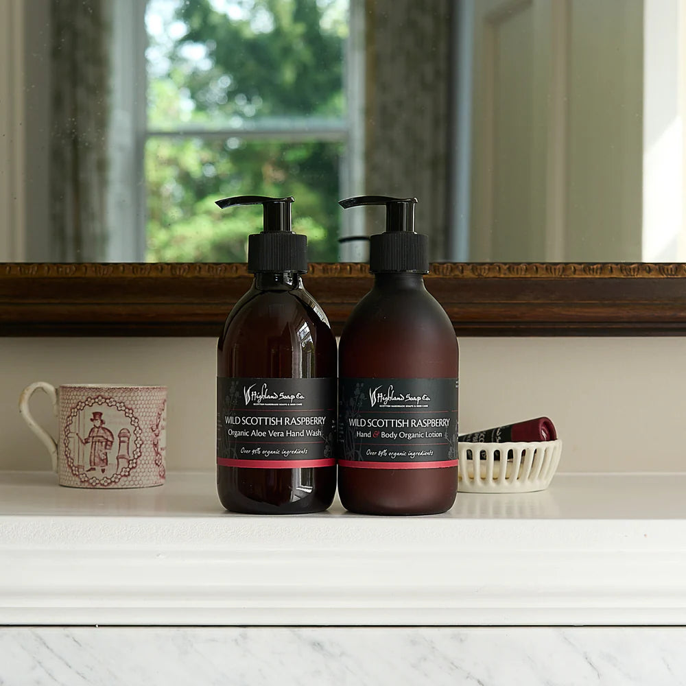 Two brown bottles of Highland Soap Company products with black labels on a white surface, with a cup and small basket in the background