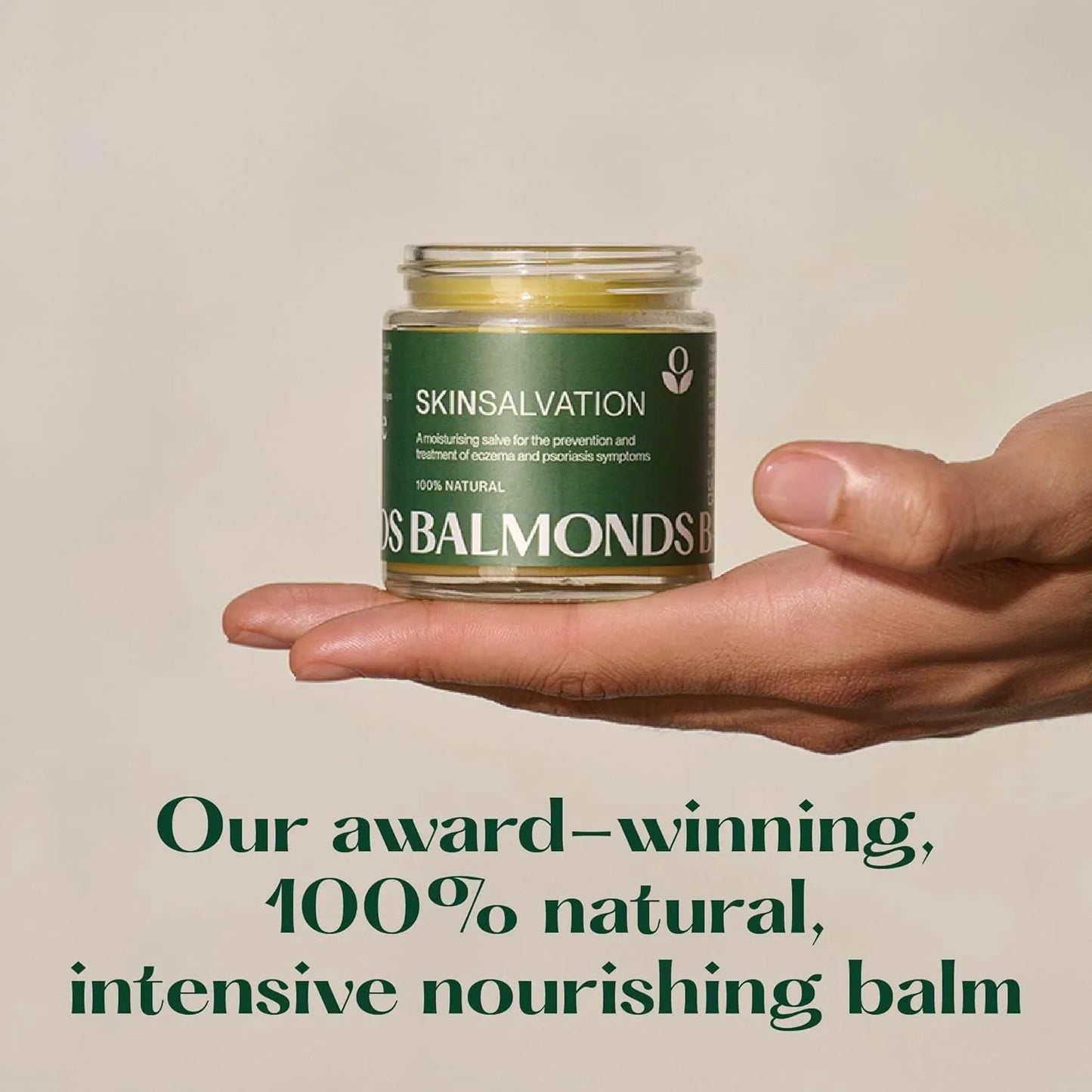 Hand holding a jar of Balmonds Skinsalvation balm against a beige background