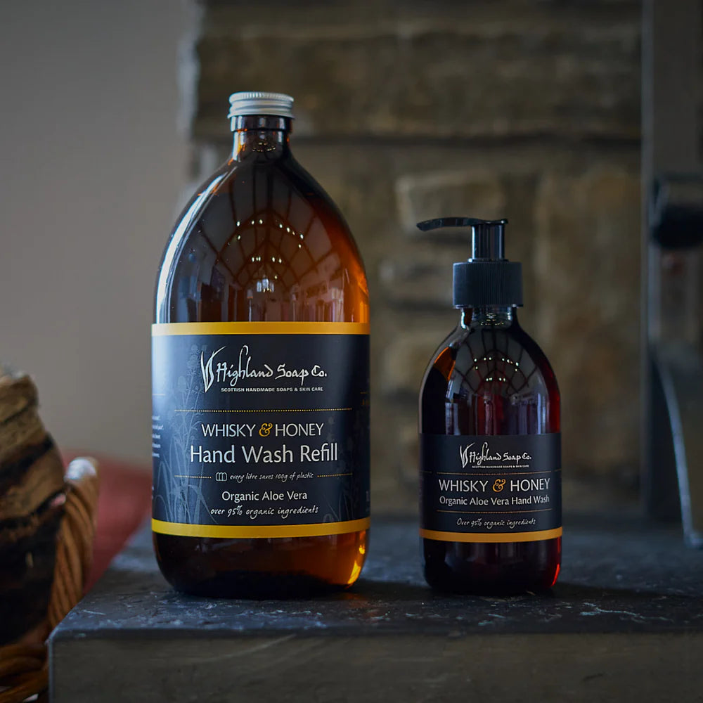 Two bottles of Highland Soap Company Whisky & Honey Hand Wash on a stone surface with a blurred background
