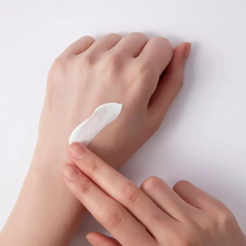 Hand applying a small amount of white cream to another hand on a light background