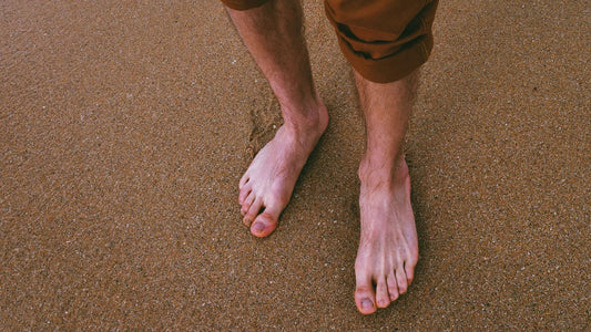 Man on sandy beach with brown shorts standing in dry bare feet