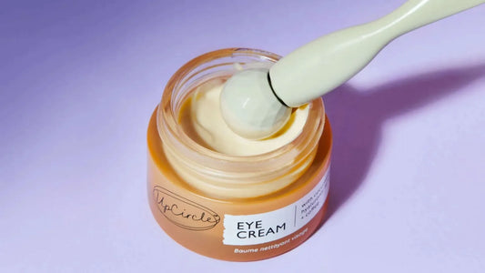 UpCircle Eye Cream with eye tool resting inside it on purple background