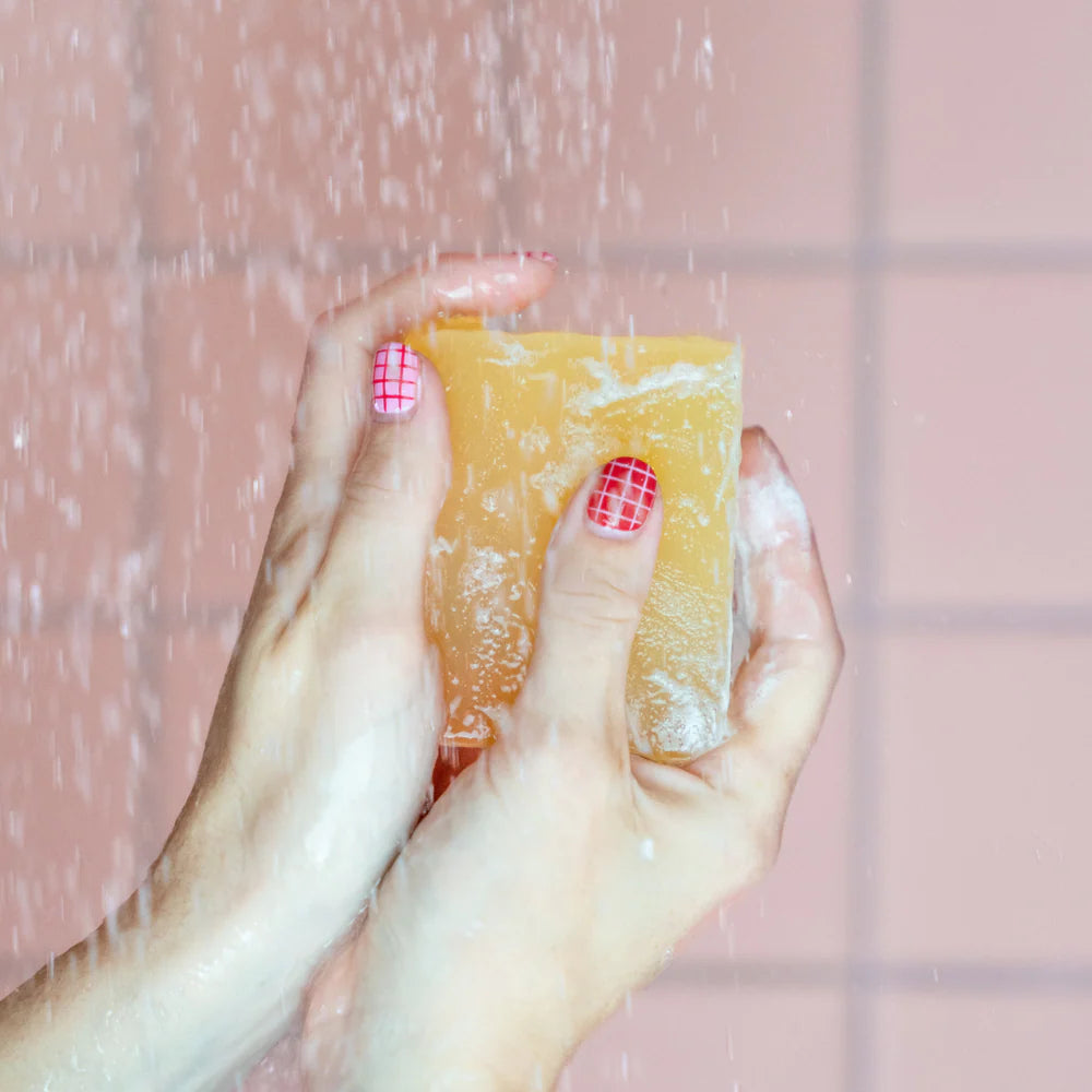 Hands holding a bar of Lemongrass & Ginger Soap under running water in a shower