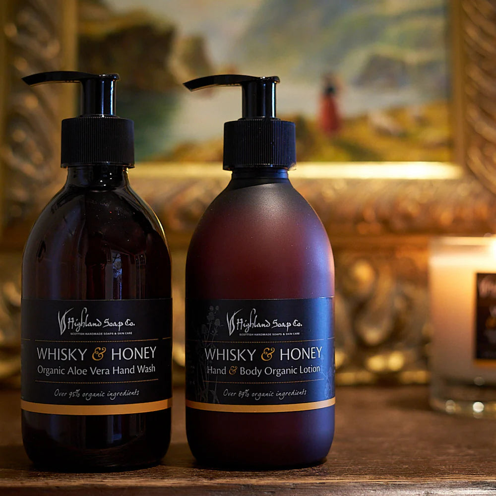 Two bottles of Whisky & Honey hand wash and lotion on a wooden surface with a blurred background