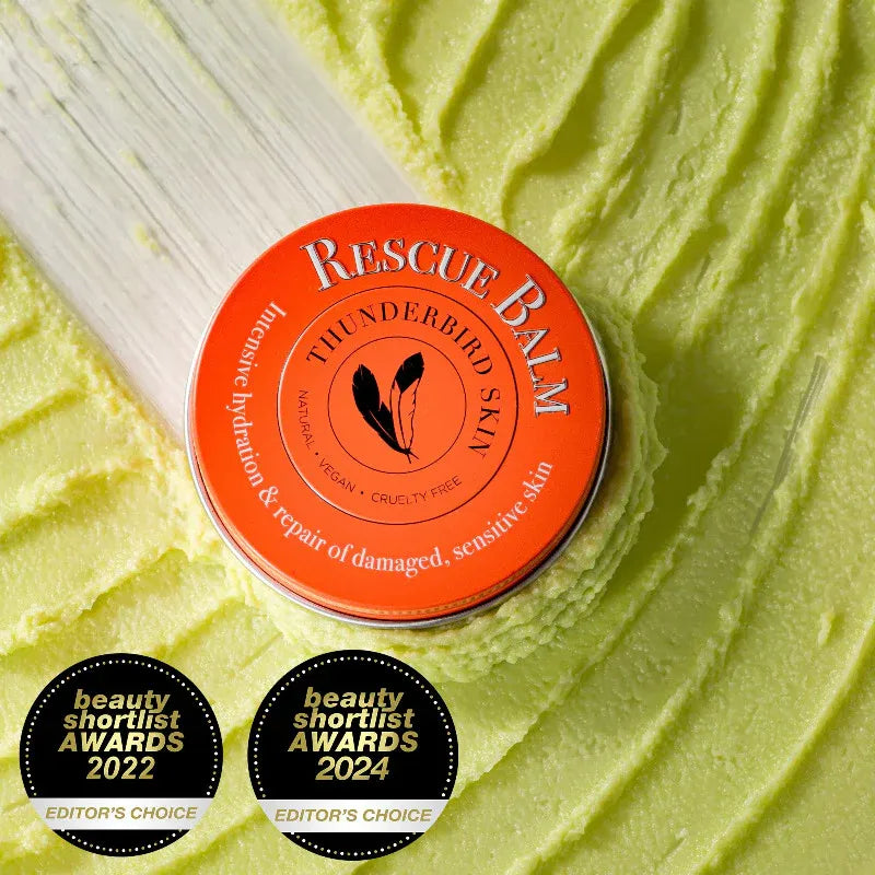 Orange tin of 'Rescue Balm' on a green textured background with awards below.