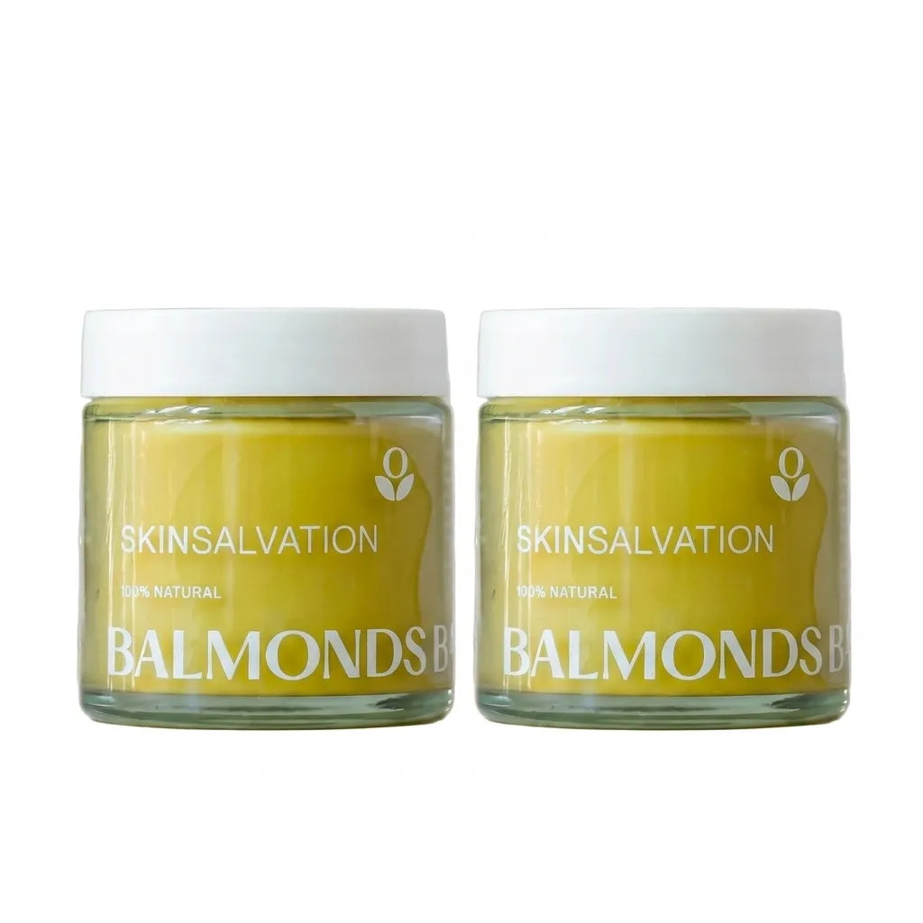 Two jars of SKINSALVATION Balmonds cream with a pale yellow cream visible through clear glass jars and white lids, set against a plain white background.