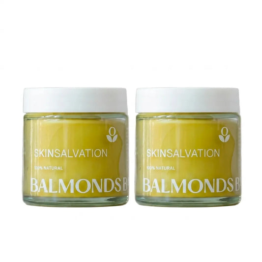 Two jars of SKINSALVATION Balmonds cream with a pale yellow cream visible through clear glass jars and white lids, set against a plain white background.